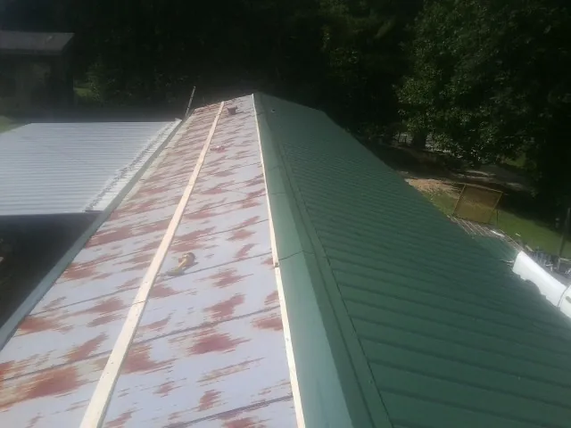 Old rusted panels beside newly installed green metal roofing — Wind Damage Roof Repair by Roofing Brothers in Cooperstown