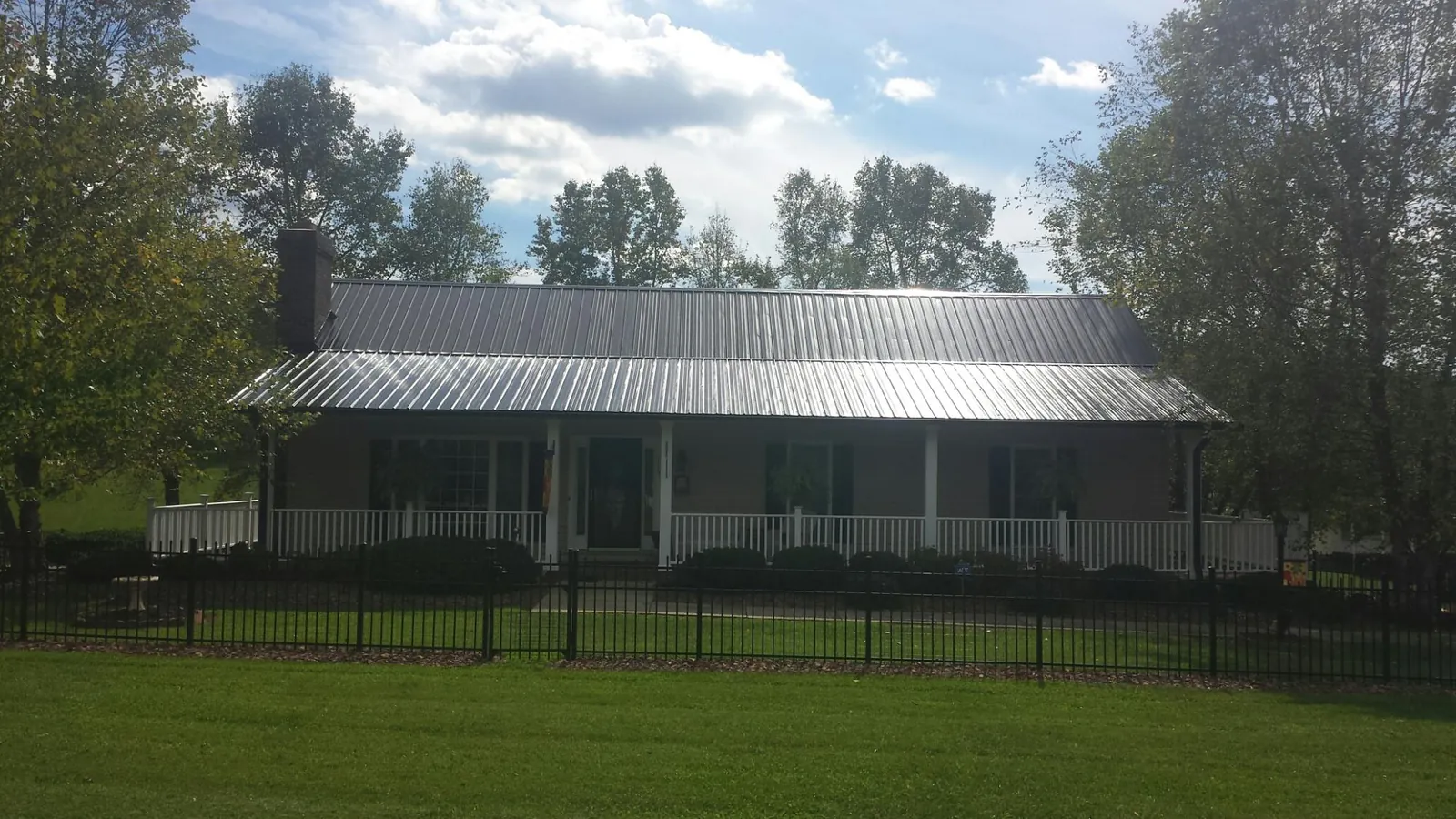 Gray metal roof on a brick ranch with a full width front porch — Gutter Guard Installation work by our crew in Cooperstown