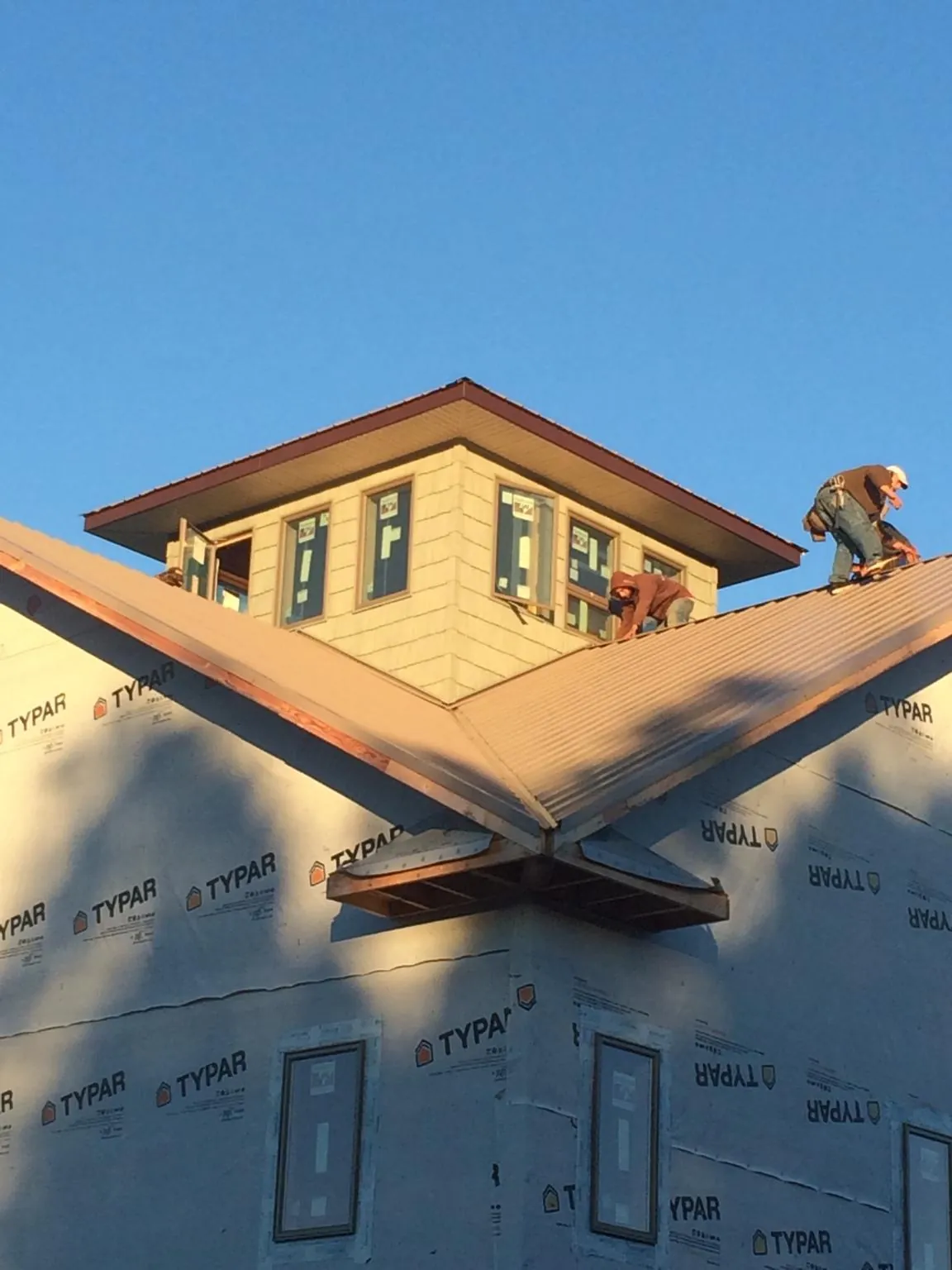 Roofers working around a rooftop cupola on a new metal roof at sunset — Roof Waterproofing in Cooperstown by Roofing Brothers
